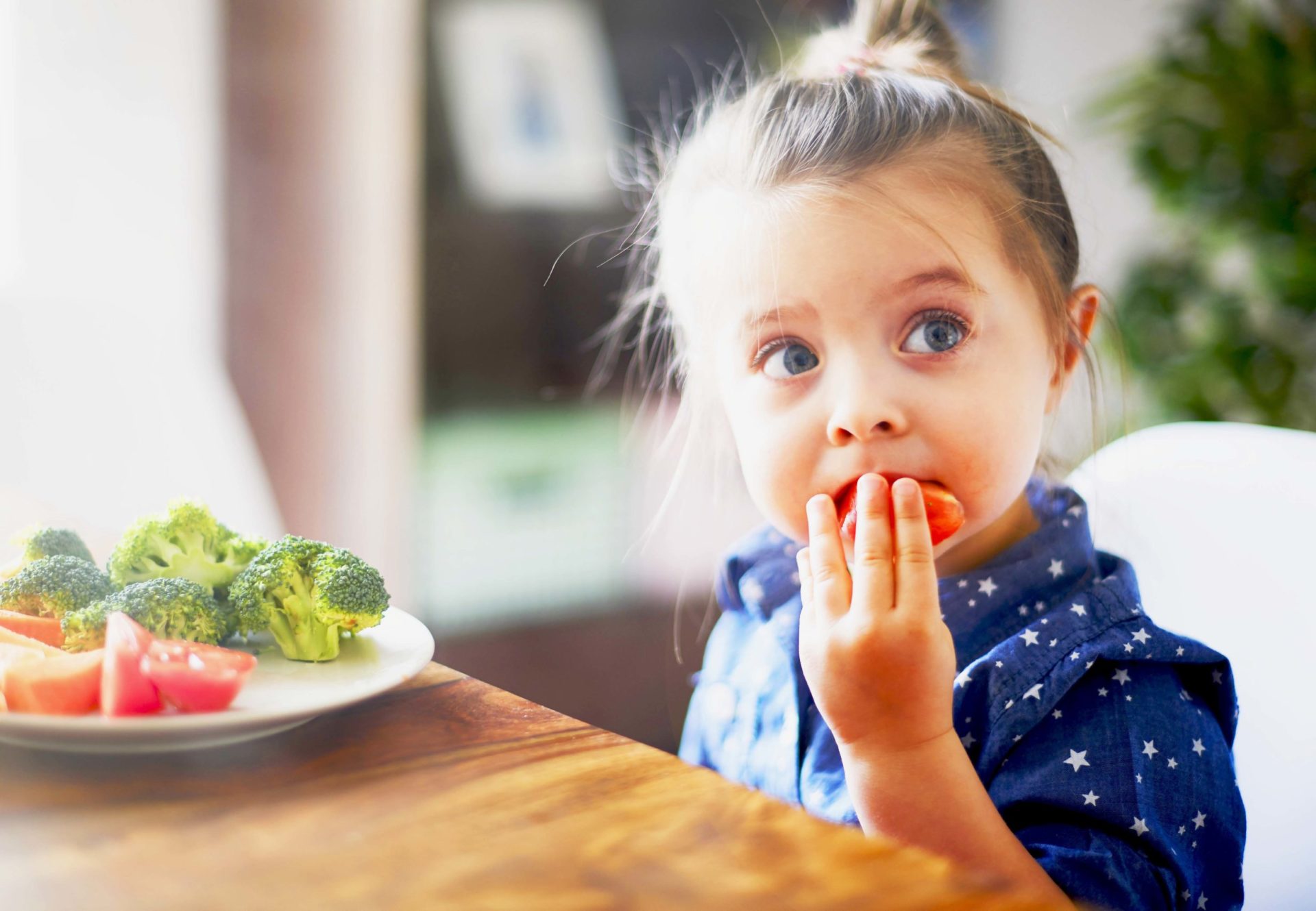 Young girl eating vegetables at kitchen table