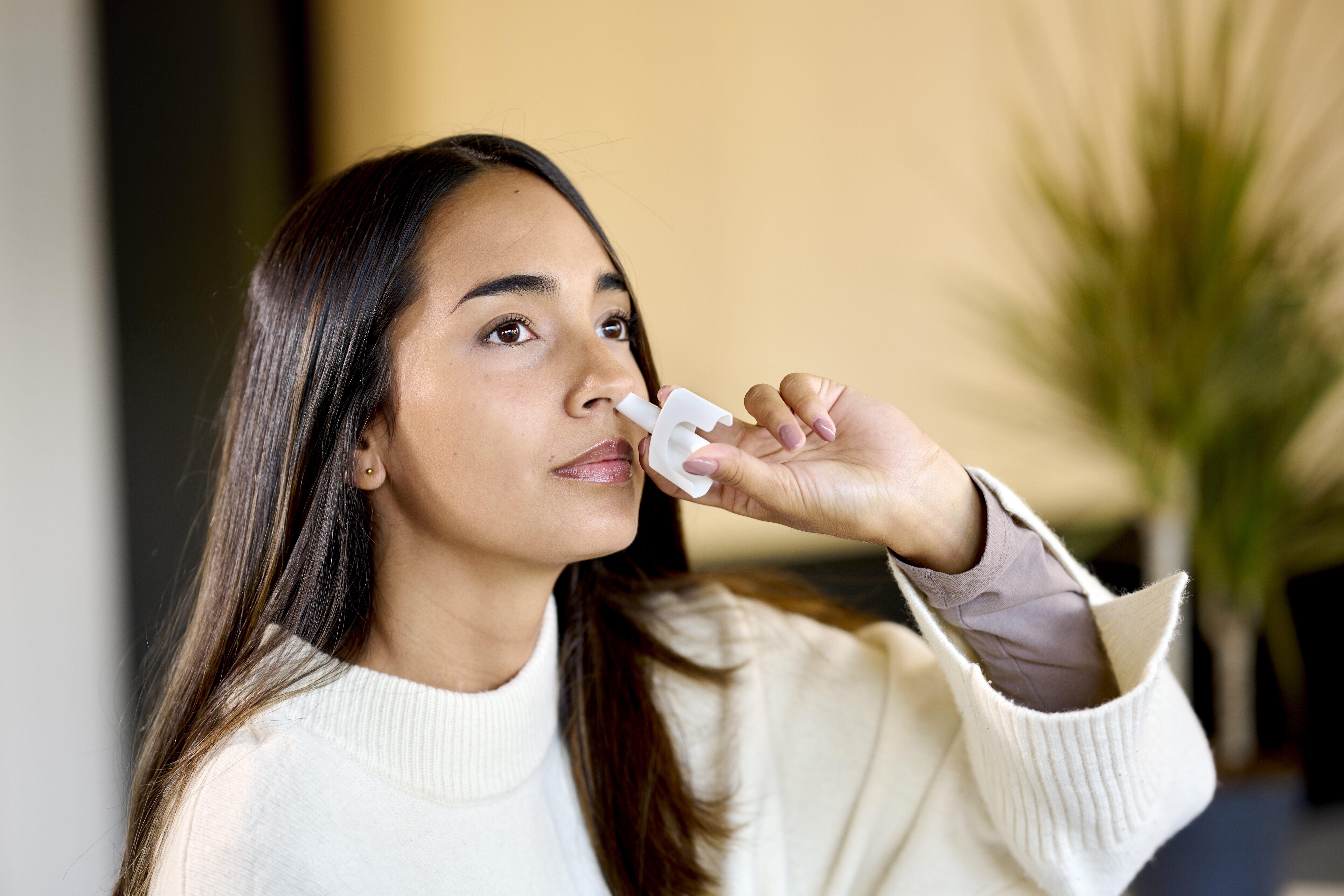 Woman in white jacket administers a single precise dose from an Aptar Unidose liquid nasal spray device zoom view