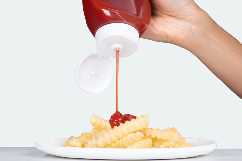 Ketchup being squeezed onto french fries on a white plate