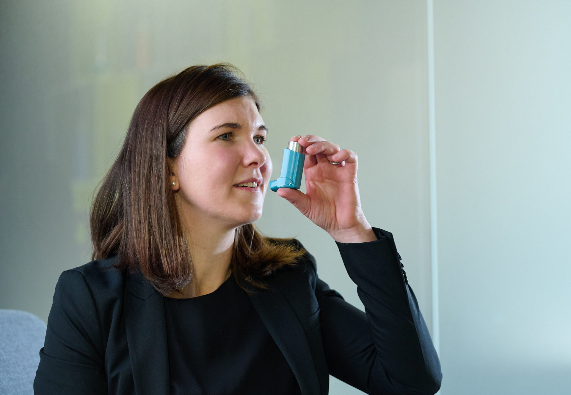 Woman with brown shoulder length hair in brown sweater holding blue inhaler containing Aptar inhaler metering valve.