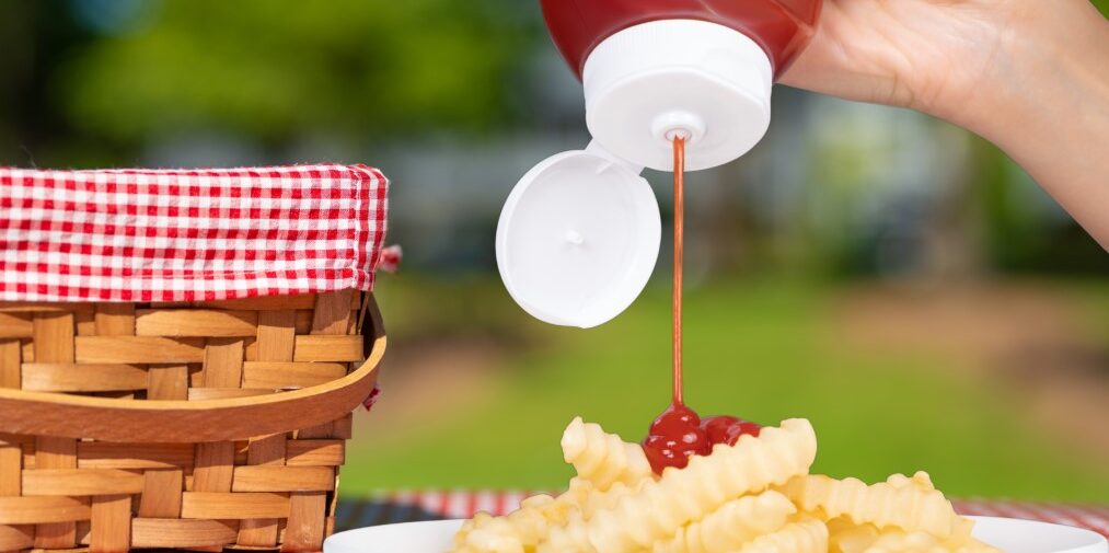 Ketchup being squeezed onto plate of fries in picnic setting
