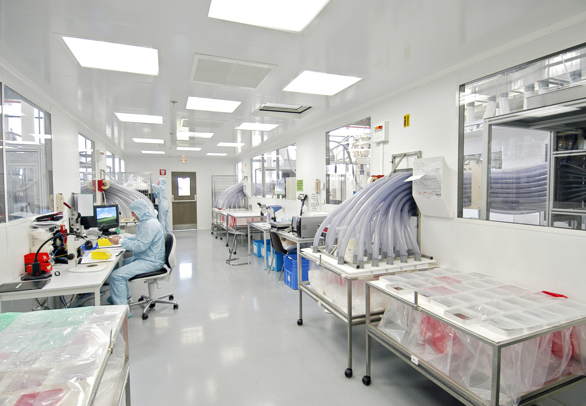 Two technical workers wearing full blue gowning with head covering working in nasal device manufacturing and inspection.